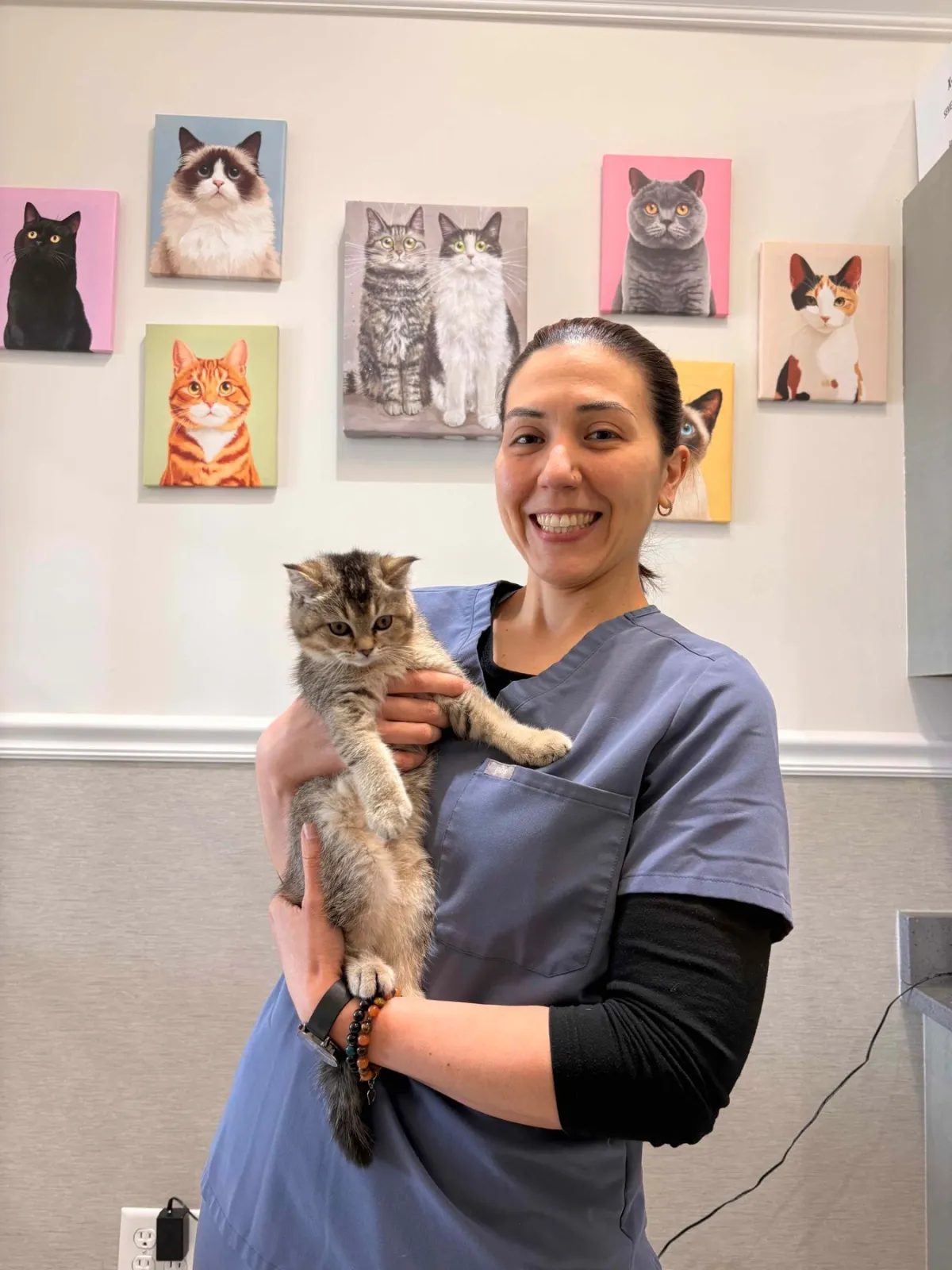 Smiling veterinarian in scrubs holding a kitten in a bright clinic.